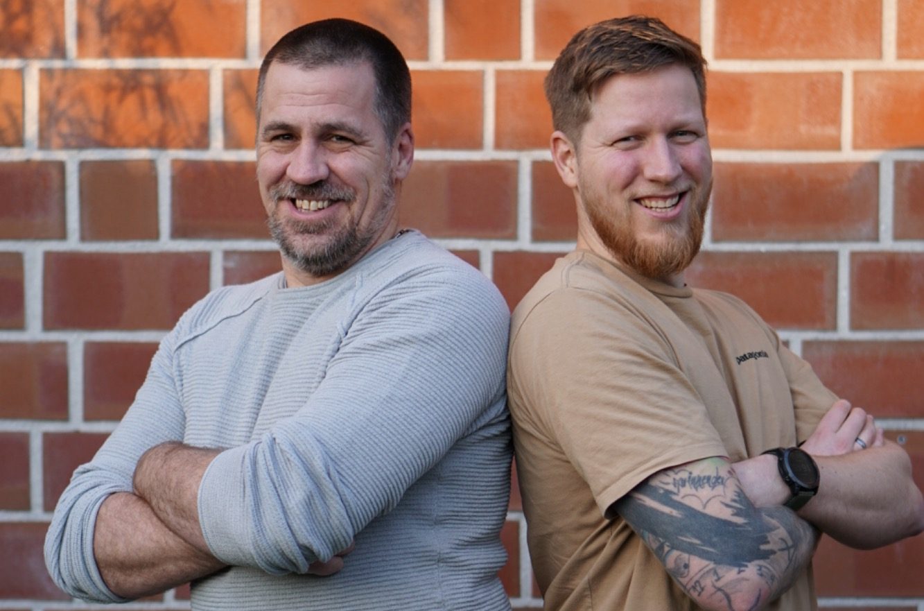 Timo und Pasal Elbers Timo und Pascal Elbers (Kanalbrüder) stehen Rücken an Rücken, lächeln und tragen lässige Kleidung.